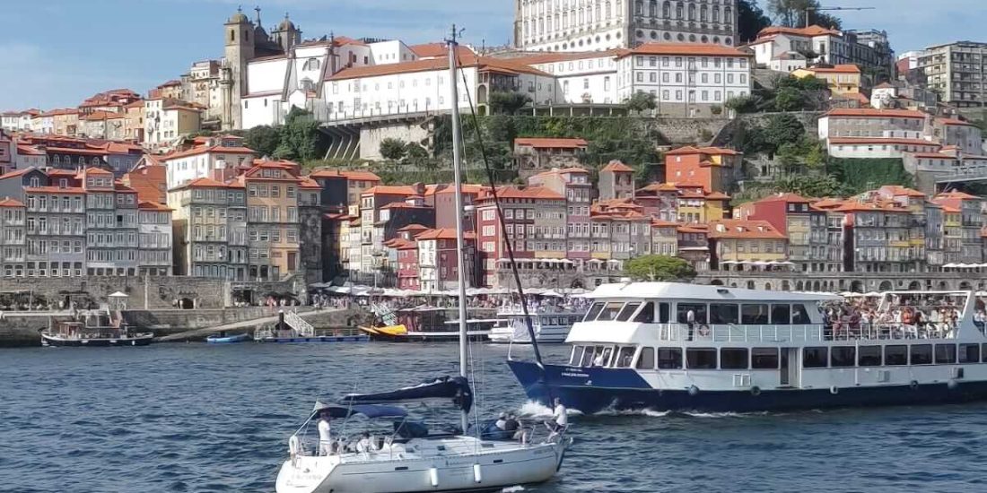 Image of the Gaia quay on a sunny day, with boats on the Douro river. Get to know Porto