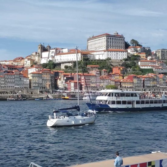 Image of the Gaia quay on a sunny day, with boats on the Douro river. Get to know Porto