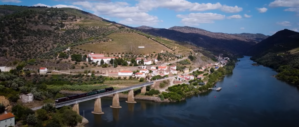 Comboio histórico passando pelo Rio Douro com as vinhas ao fundo.